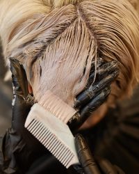 Close up of hairstylist applying bleach or dye to hair strands in beauty salon, copy space