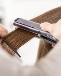 Hairdresser straightening long brown hair with hair irons.